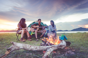 Group of travelers camping and doing picnic and playing music together. Mountain and lake background. People and lifestyle. Outdoors activity and leisure theme. Backpacker and Hiker. Dawn and twilight
