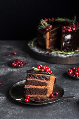 Glazed chocolate cake decorated with cranberries and rosemary, on black wooden serving board on...