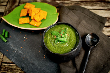 Green broccoli soup, on a gray stand, and a wooden background. Rustic style. Simple, nutritious vegetarian food. Decorated with seeds. With a linen napkin. With crackers or cereal loaves