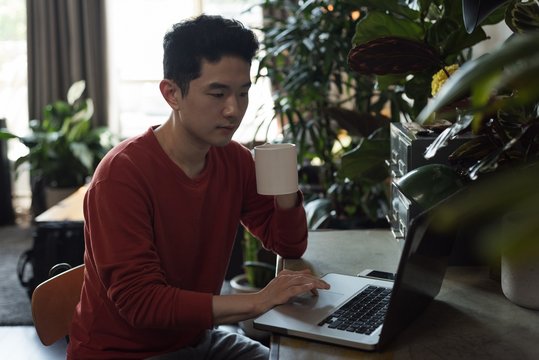 Man having coffee while using laptop in living room