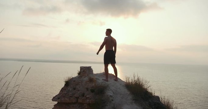 Young man topless standing on the edge of a cliff enjoying the nature