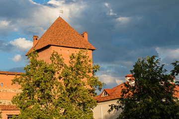 A powerful tower of the Lida castle from red brick and stone lit with  the sun against a beautiful but stormy sky