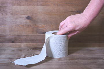 Hand reaches for toilet roll on wooden background