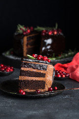 Glazed chocolate cake decorated with cranberries and rosemary, on black wooden serving board on anthracite stone table