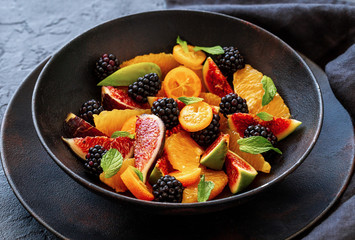 Fruit salad with fresh blackberries, figs and kumquats on a plate on black background. Healthy eating.