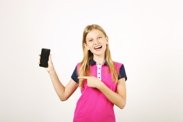 Portrait of casual teen age girl with long natural blond hair, index finger pointing at blank screen cell phone. Happy young female holding smartphone, showing display. White background, copy space