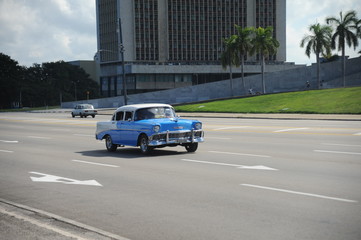 Brightly colored classic American cars serving as taxis pass on the main street in front of the Capitolio building in Central Havana, Cuba