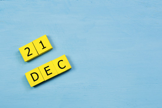DEC 21, yellow cube calendar on blue wooden surface with copy space