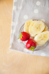 strawberry and banana on a glass plate on a wooden background.