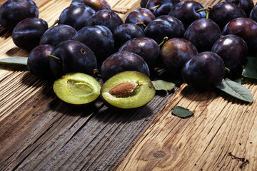 Plums on rustic background. Half of blue plum fruit. Many beautiful plums with leaves