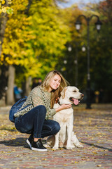Beautiful young blonde is walking in the park with her labrador in the park in the fall. The woman crouched beside her retriever.