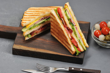 Classic club sandwich with ham and bacon on a wooden board. Next cup is a mixture of pickled...