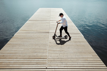 Photo of modern man with electric scooter at a wooden pier