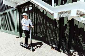 Modern man dressed white shirt and black pants standing at the street with electric scooter