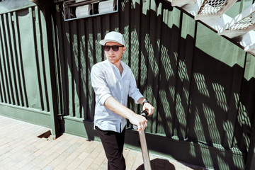 Modern man dressed white shirt and black pants standing at the street with electric scooter