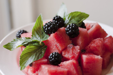 Blackberries, cubes of watermelon, mint leaves on a white plate closeup