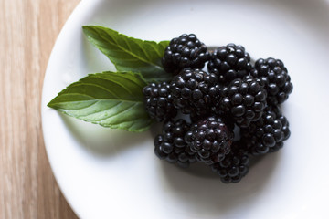 Berries of a blackberry, mint leaves on a white plate closeup