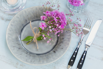 Rustic table setting with pink flowers and candle on light wooden table.