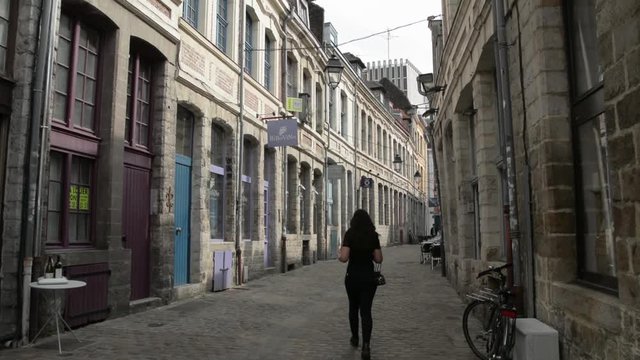 People walking into a narrow paved street, in Lille, France.