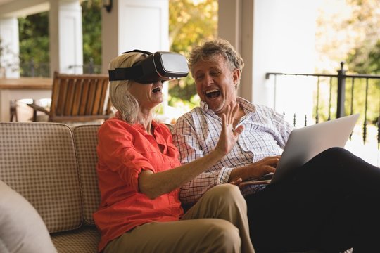 Senior couple using laptop and experiencing VR headset in porch