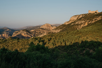 Rocky mountains with the ancient castle in the distance with the giant shadow on the front in the evening in Spain. El Castillo de Chirel.
