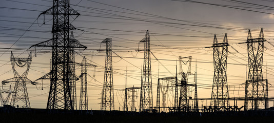Electricity transmission pylon silhouetted against sunset sky. High voltage electric tower line
