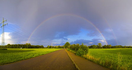 Rainbow after a thunderstorm over a road between green Meadows