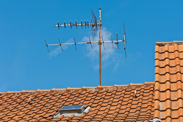 Eine alte Fernsehantenne auf einem Dach aus Tonziegeln unter blauem Himmel