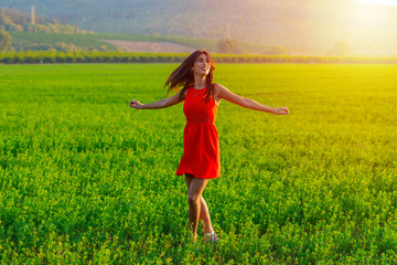 Young woman happily twirling in her summer red dress. Girl Spinning in a green field at sunny day....