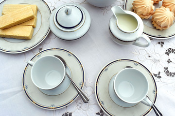 Served coffee table. On the table, a coffee pot, two cups and saucers, a milkman, a sugar bowl, small spoons, a plate of marshmallows and a plate with waffles. 