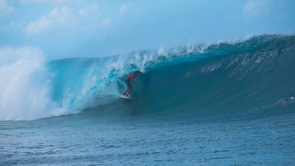 Awesome young surfer rides a beautiful emerald barrel wave in sunny Tahiti.