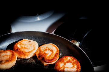 pancakes of cottage cheese are fried in a pan in the dark