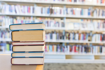 Small stack of various sized books on library desk with shelves of books behind