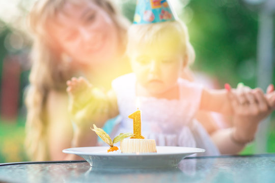 capkake with a candle in the form of a number one, in the background a blurred family mom and daughter. happy birtday