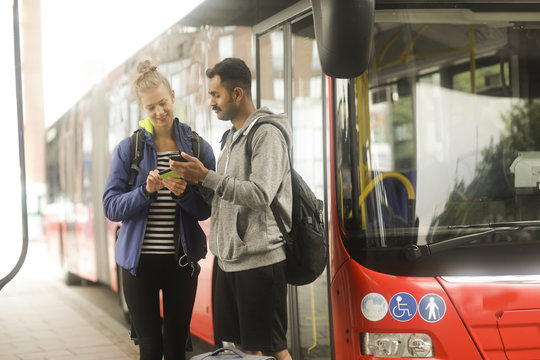 Couple standing by a bus looking at a mobile phone