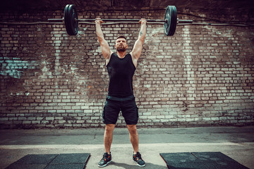 Muscular fitness man doing deadlift a barbell over his head in outdoor, street gym. Functional...
