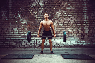 Muscular fitness man doing deadlift a barbell over his head in outdoor, street gym. Functional...