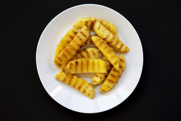 Top view, grilled pineapple wedges on a white plate over black background. Summer food. Closeup.
