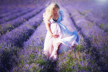 young pregnant woman in light dress walking through the lavender field