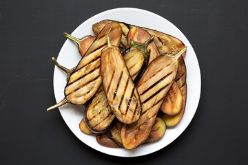 View from above, grilled eggplant on a white plate over black background. Closeup.