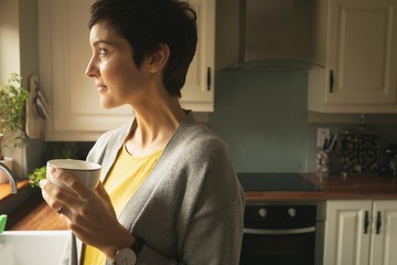Woman looking away while having coffee in the kitchen