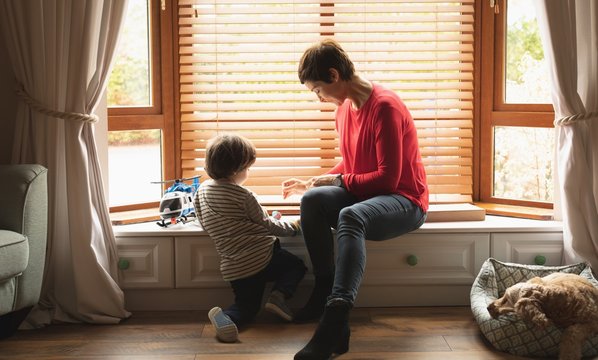 Mother playing with son on window sill in living room
