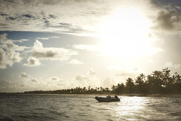 Obraz premium Boat by the sea at sunset with palm trees in the background.
