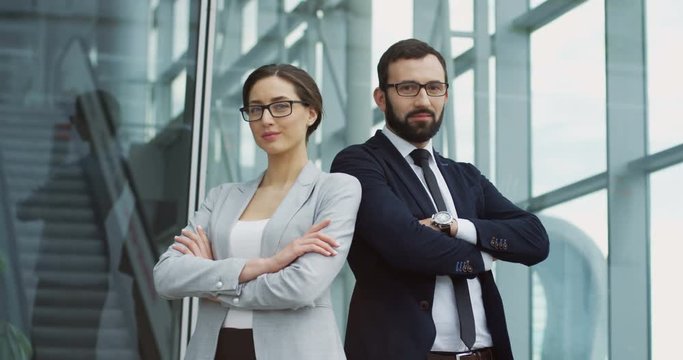 Attractive smiled man and woman in official style crossing their hands in front of them and posing to the camera at the urban office center. Portrait shot. Business team.
