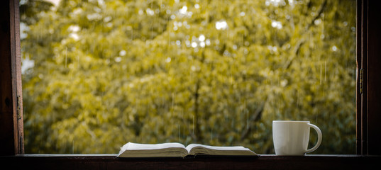 Cozy autumn still life: cup of hot coffee and opened book on vintage windowsill and rain outside....