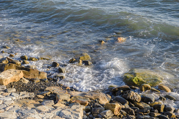 pebbles on the beach pebbles on the sea shore and waves of water illuminated by the rays of the sun.
