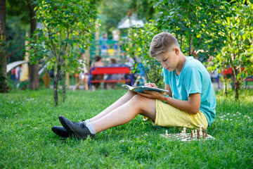 cute, smart, handsome boy in mint tshirt plays chess  in the summer park. Education concept, intellectual game.  training concept