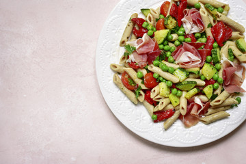Delicious whole wheat pasta penne with vegetables ( tomato, zucchini, grilled bell pepper, green pea ) and prosciutto.Top view with copy space.