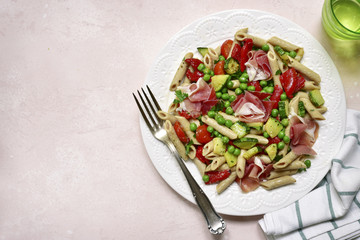 Delicious whole wheat pasta penne with vegetables ( tomato, zucchini, grilled bell pepper, green pea ) and prosciutto.Top view with copy space.
