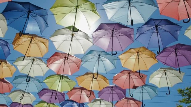 The street is decorated with colored umbrellas. Umbrellas in the sky. The sun breaks through the umbrellas.